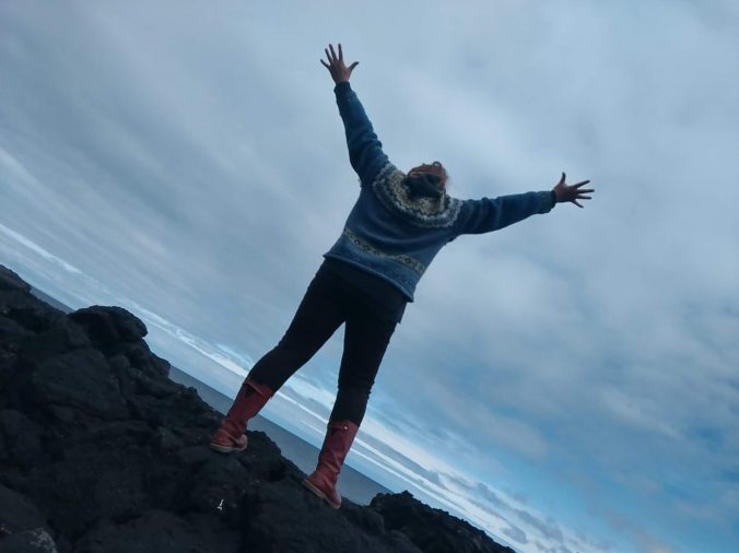 Isländerin von hinten im Island-Pullover springt hoch auf Felsen