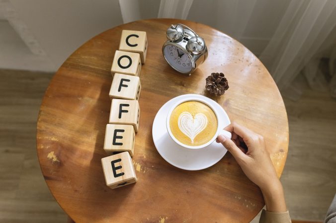Das englische Wort Coffee steht symbolisch für eine Gewohnheit, Kaffee trinken, auf einem Holztisch.